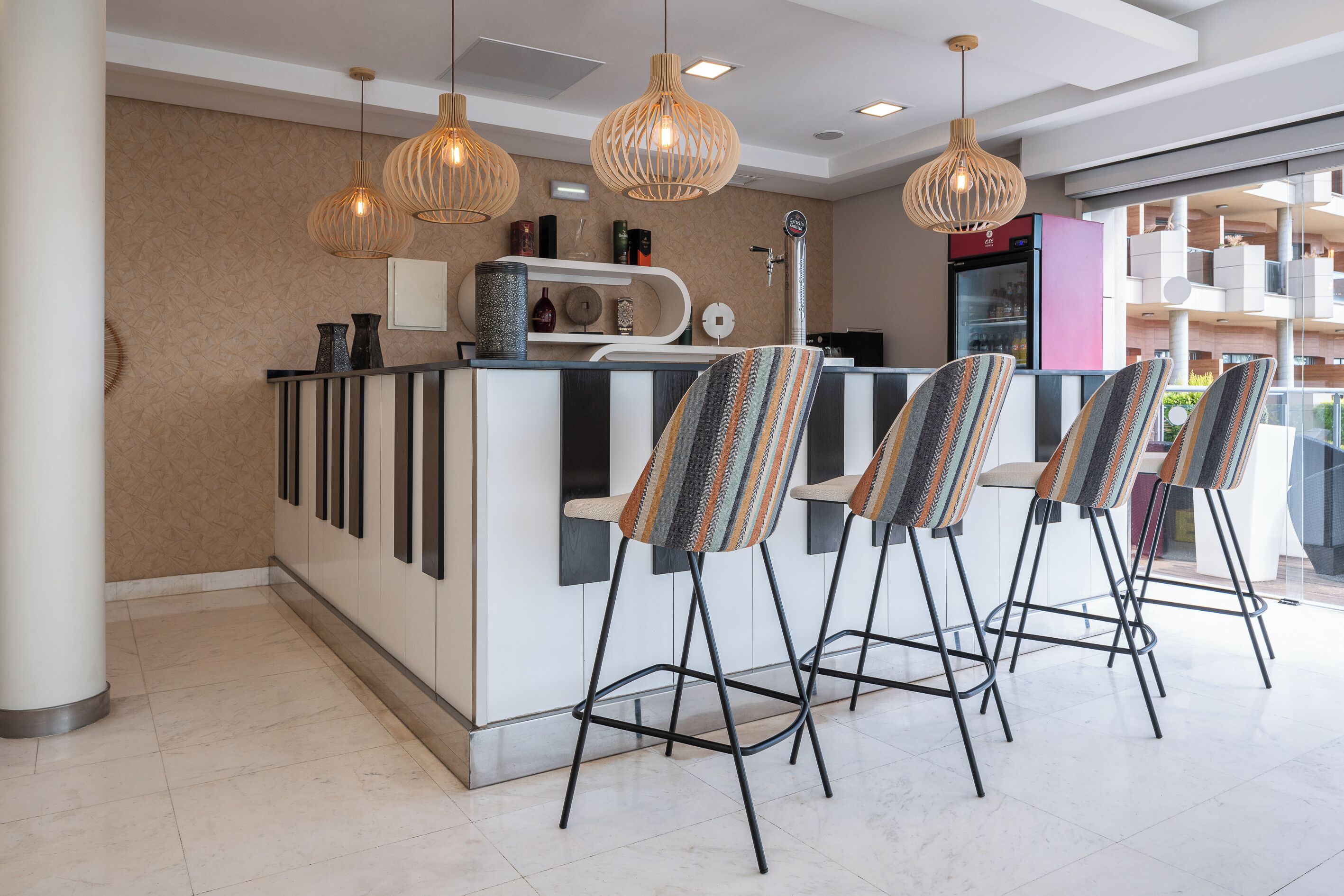 A modern bar area with three high stools, a white counter, and pendant lighting.