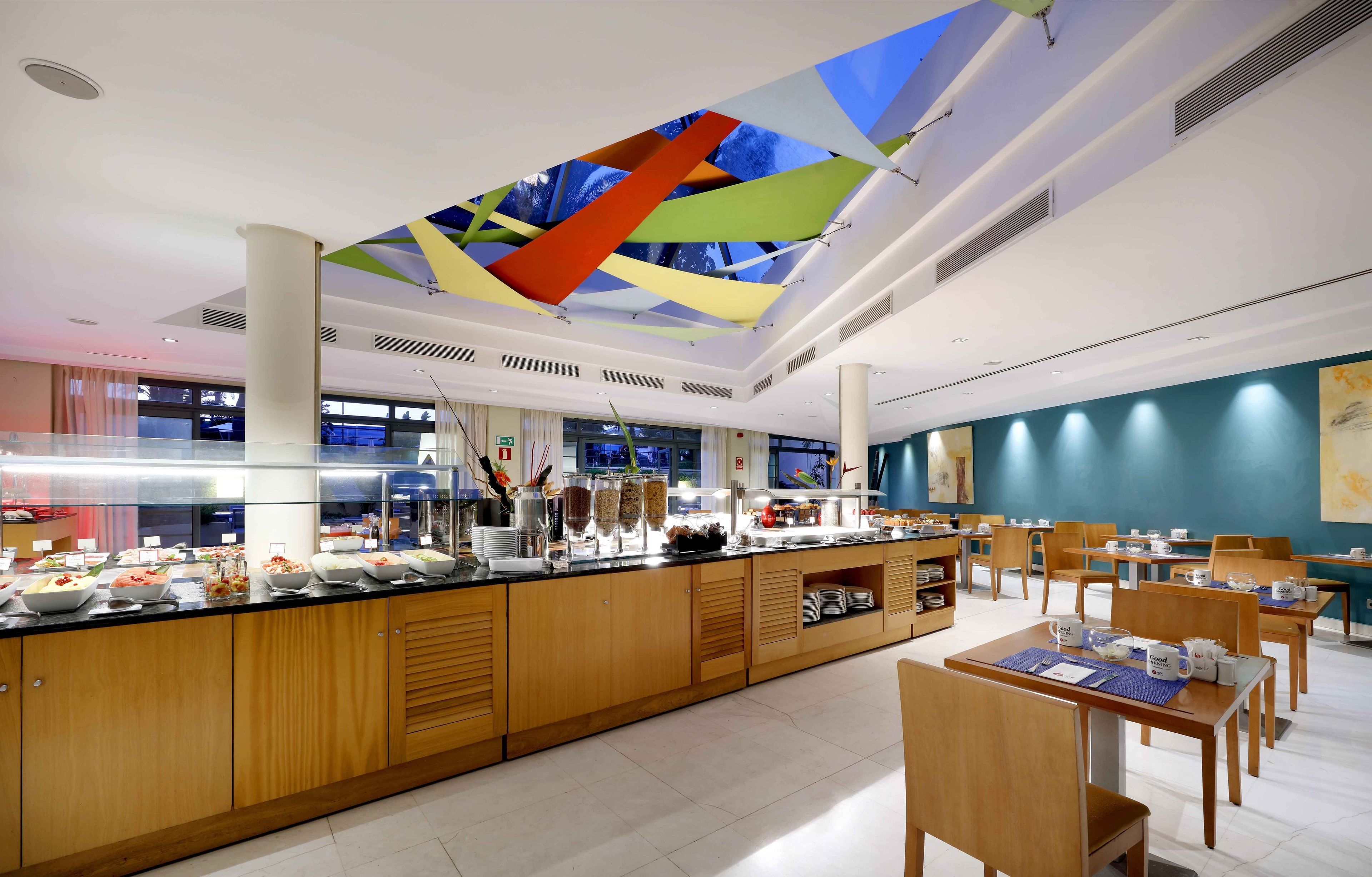 A modern breakfast area with a long counter, wooden cabinets, and a colorful ceiling design.