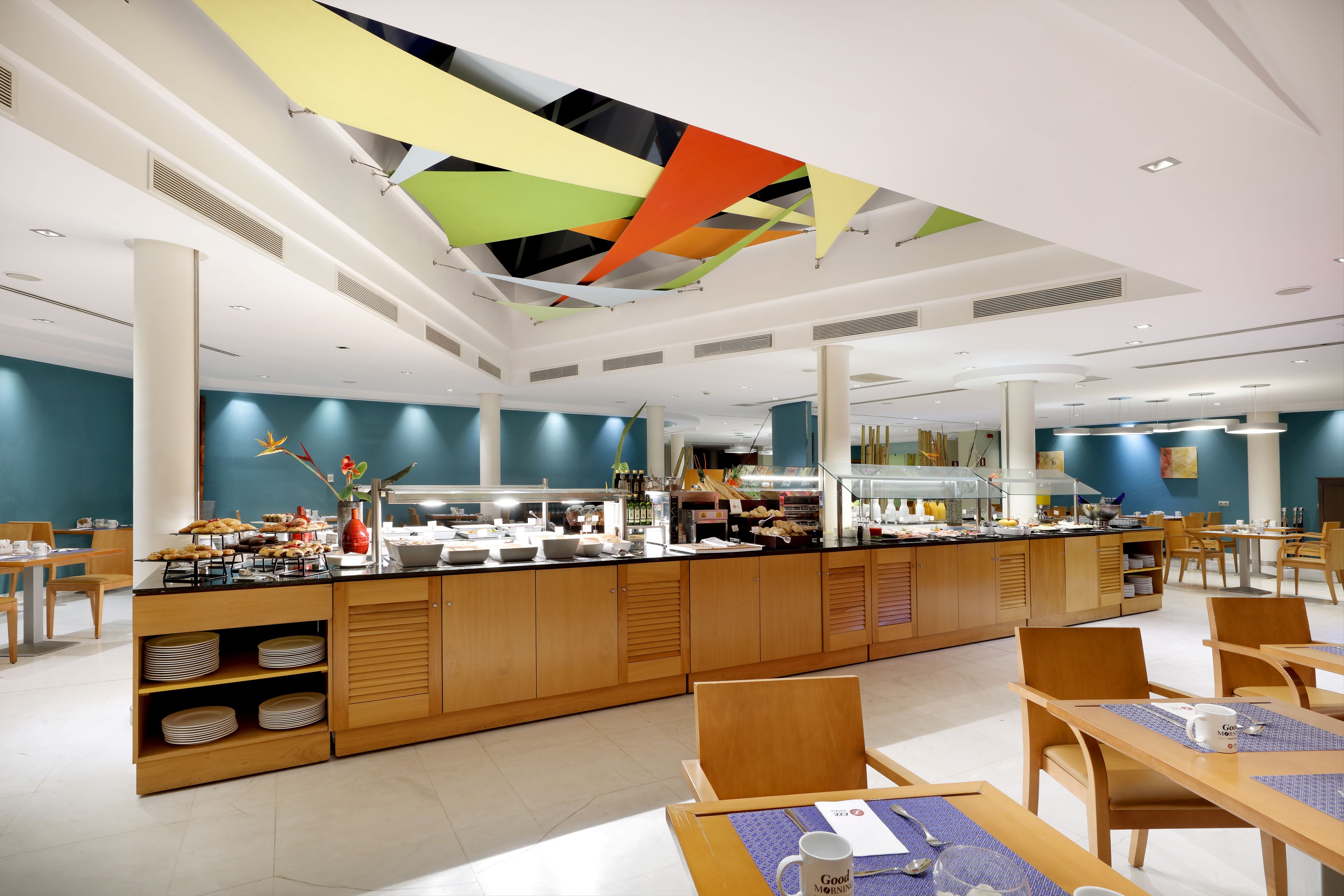 Un'area ristorazione moderna con servizio a buffet, arredi in legno e un design di soffitto colorato.