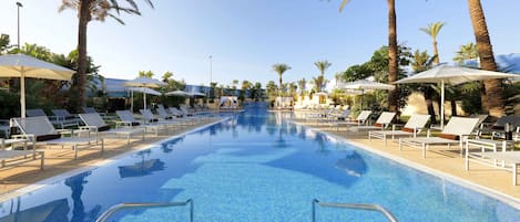 A swimming pool with lounge chairs and umbrellas, surrounded by palm trees.