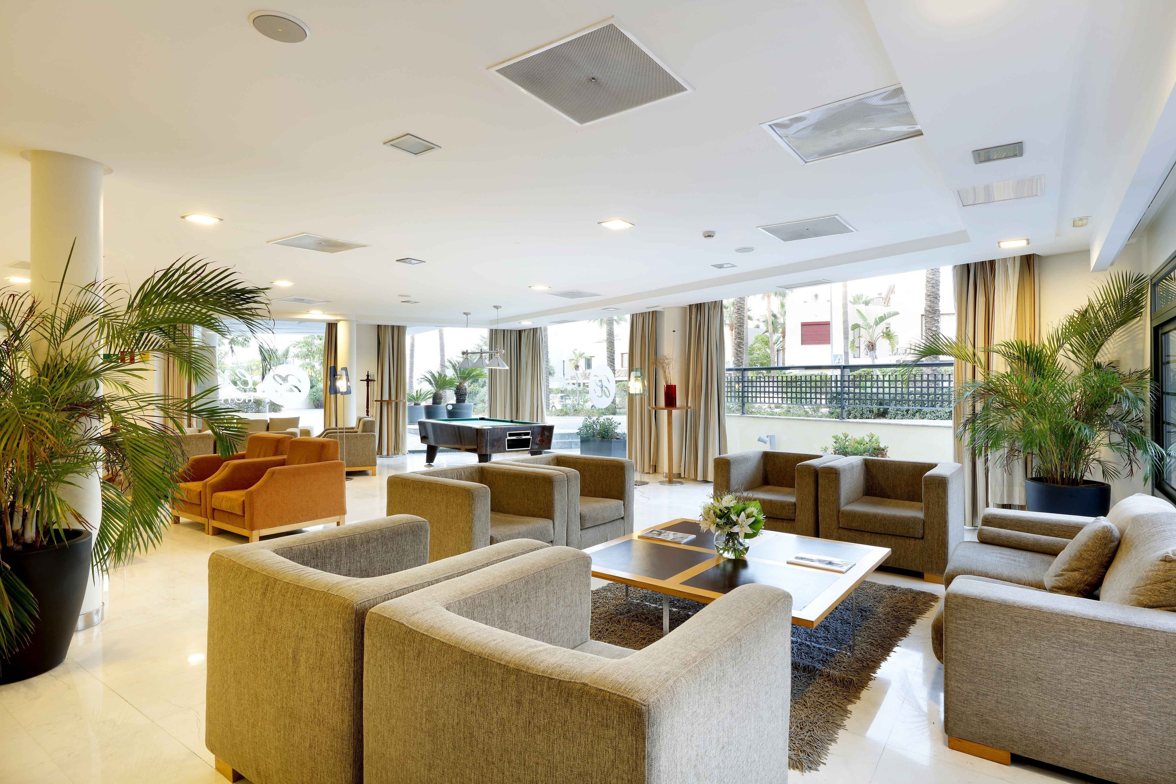 A spacious lobby with multiple seating areas, a pool table, and large windows offering a view of the outdoors.