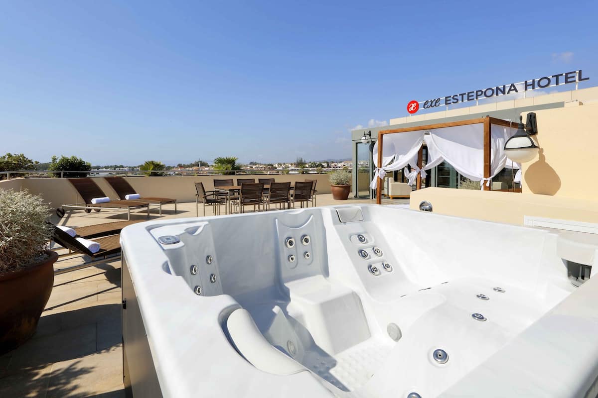 A rooftop terrace with a hot tub, lounge chairs, and a view of the city.