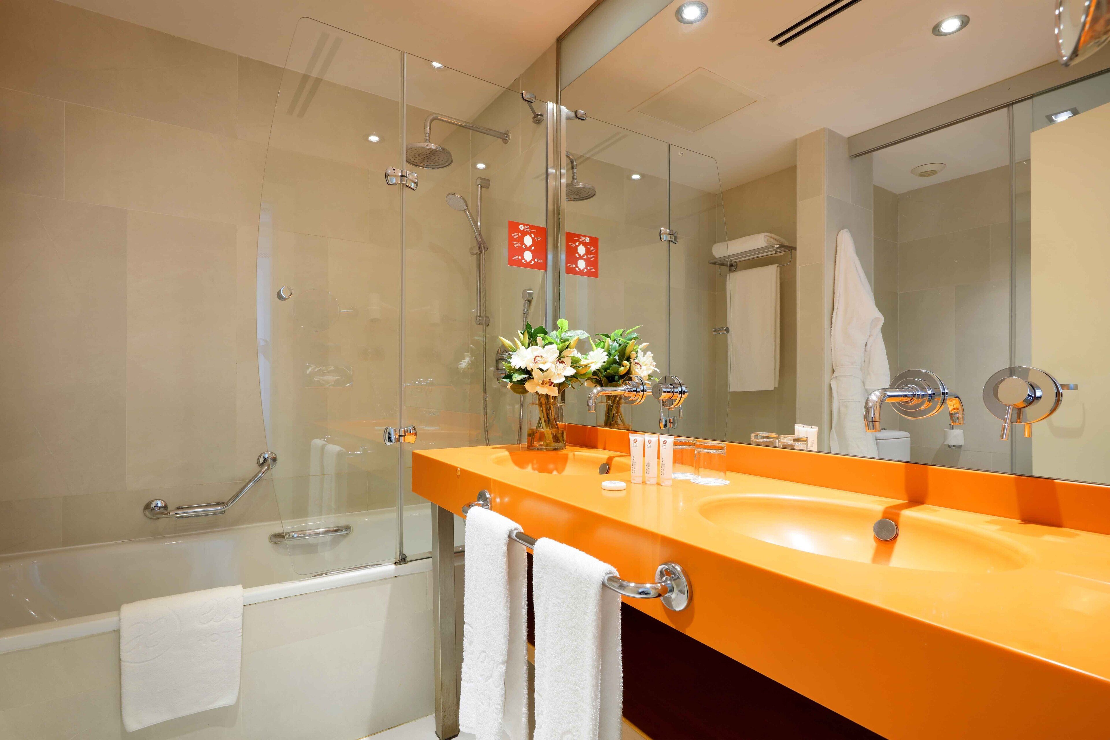A modern bathroom with a glass shower enclosure, a large mirror, and an orange sink.