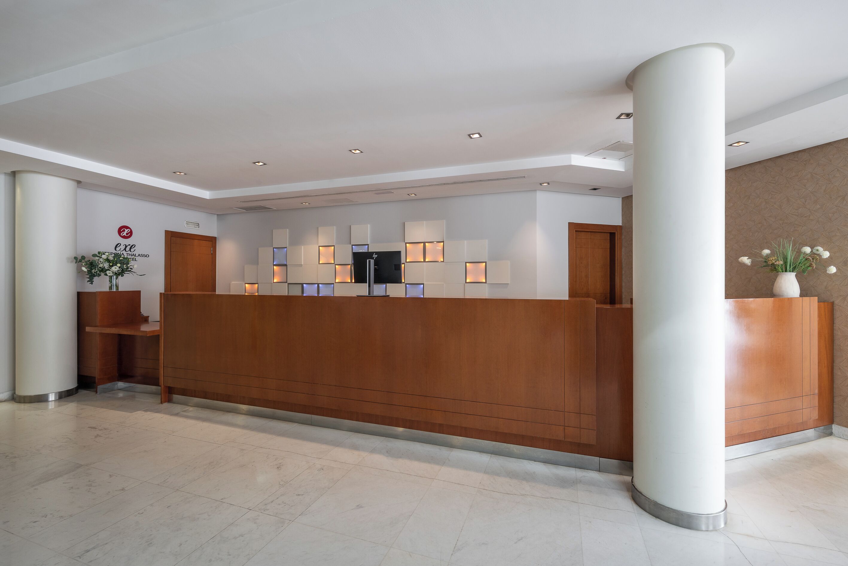 A reception desk with a wooden finish, a white wall with a logo, and a column.