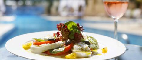 A plate of food with a glass of rosé wine on a table by a pool.