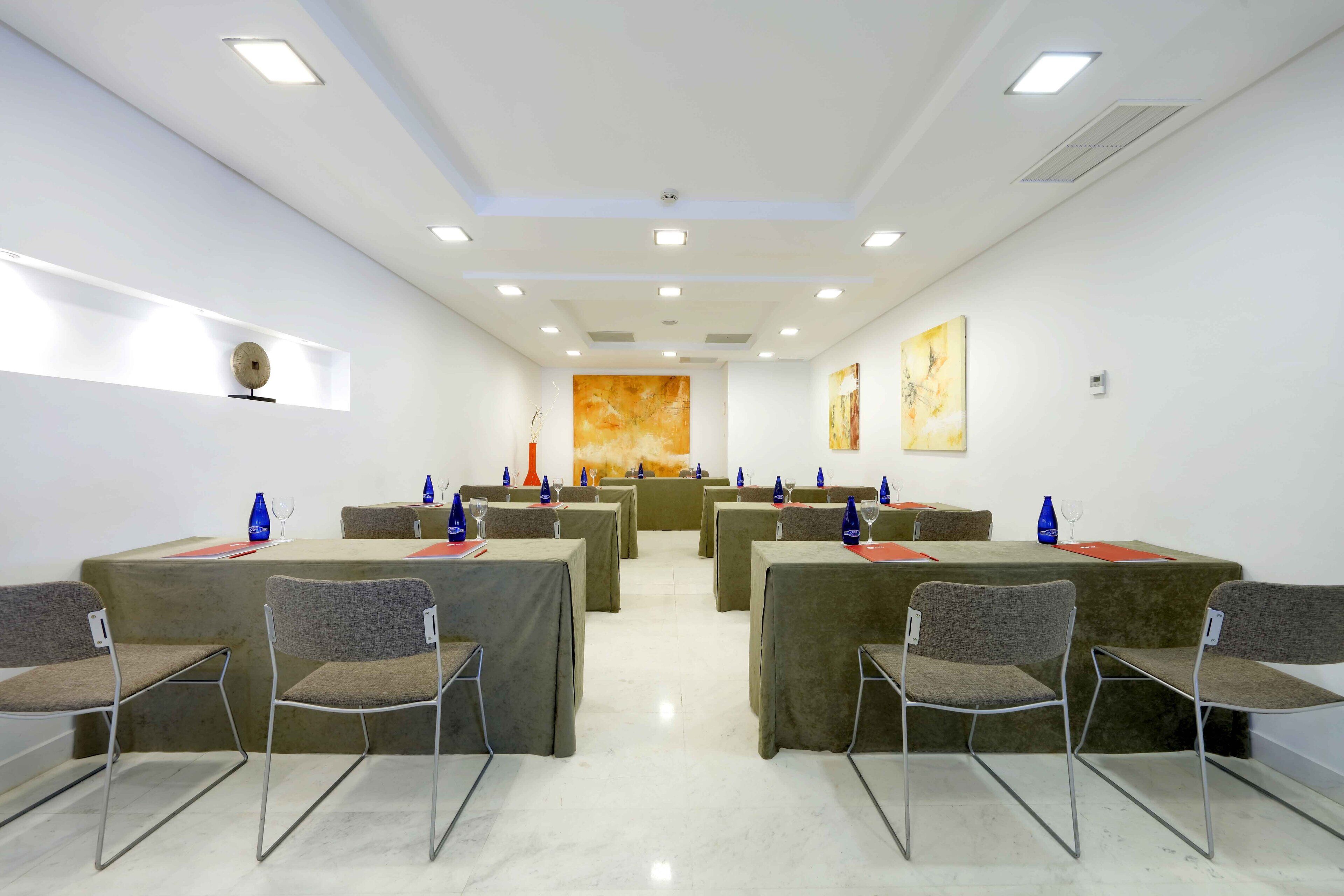 Un salón de conferencias con varias mesas y sillas, equipado con copas y manteles individuales rojos.