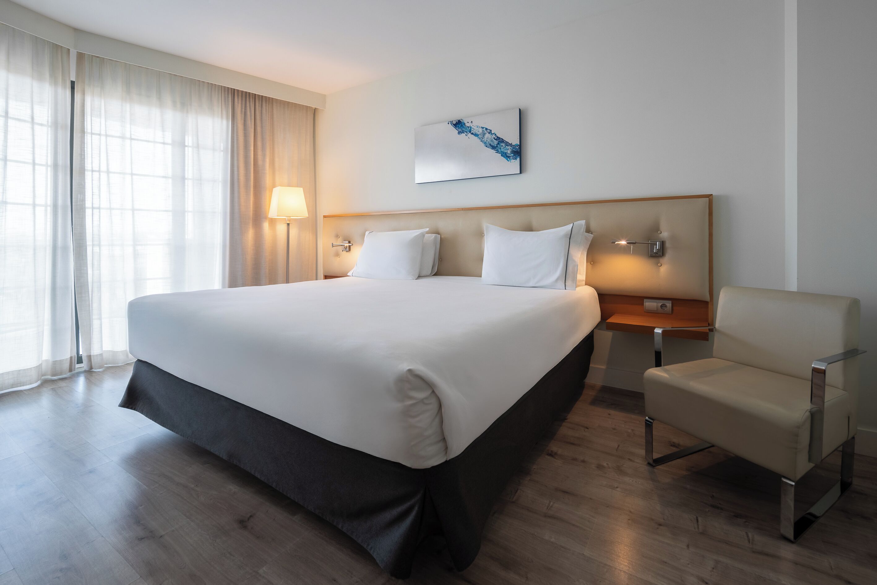 A hotel room with a large bed, a chair, a bedside table, and a lamp.
