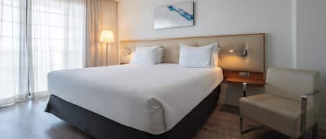 A hotel room with a large bed, a chair, a bedside table, and a lamp.