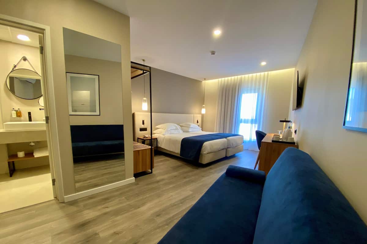 Una habitación de hotel moderna con una cama, un sofá azul, un escritorio y un baño con lavabo y espejo.