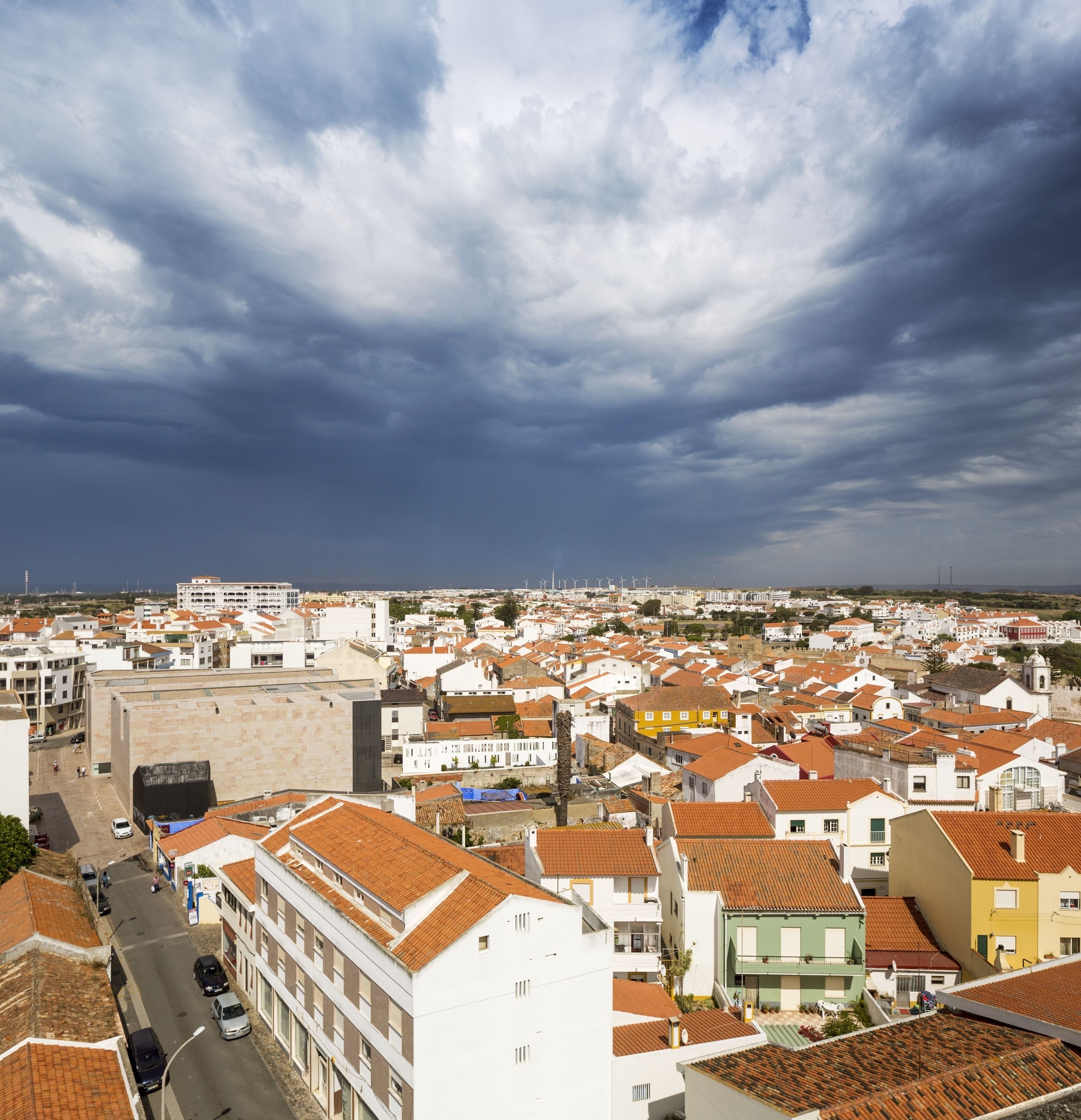 A coastal town with a mix of traditional and modern architecture, featuring terracotta-roofed buildings and a prominent white building with a flat roof.