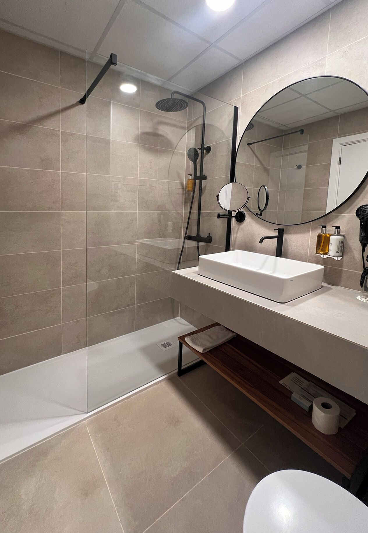 Un baño moderno con cabina de ducha, un espejo grande y un tocador con lavabo.