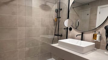 Un baño moderno con cabina de ducha, un espejo grande y un tocador con lavabo.