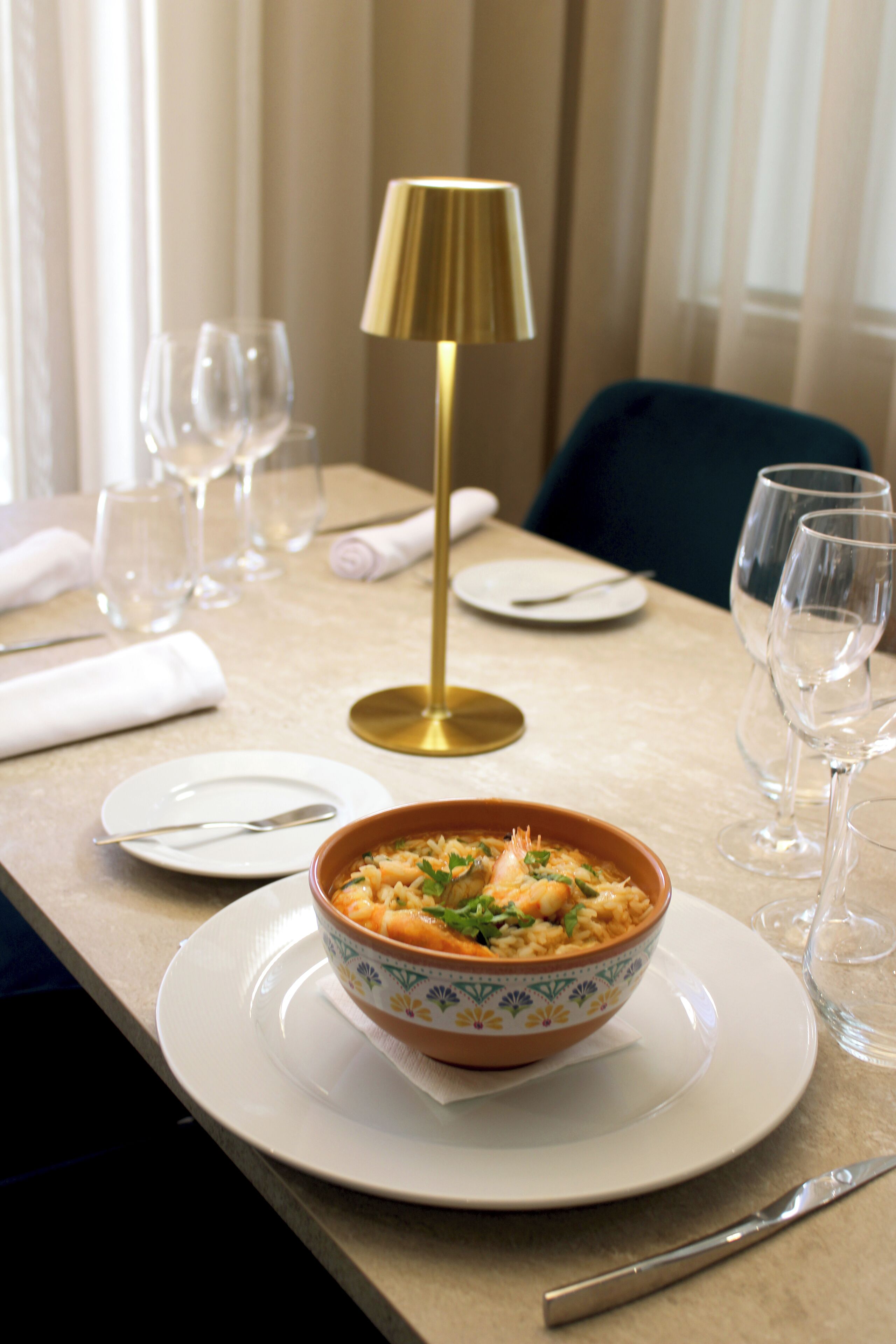 Una mesa de comedor con un plato de comida, una lámpara dorada y copas de vino vacías.