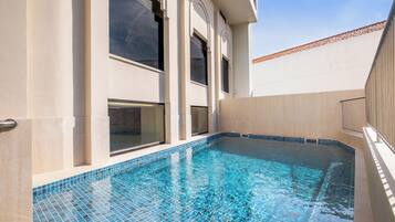 A swimming pool with clear blue tiles, large windows, and a tiled deck area.