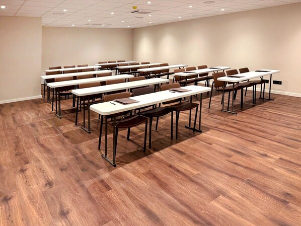 A conference room with multiple tables and chairs, wooden flooring, and a plain wall. - AP Sines (Sines)