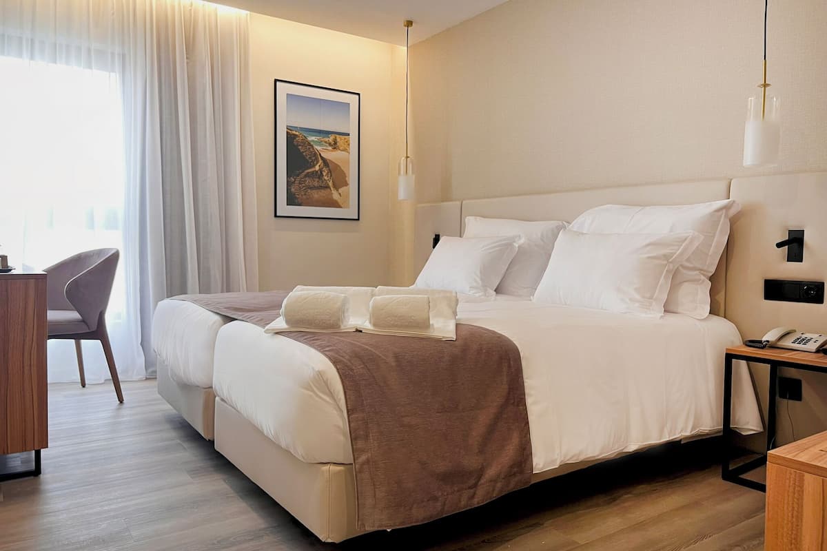 Habitación de hotel con una cama grande, un escritorio, una silla, un cuadro en la pared y una mesita de noche con un teléfono.