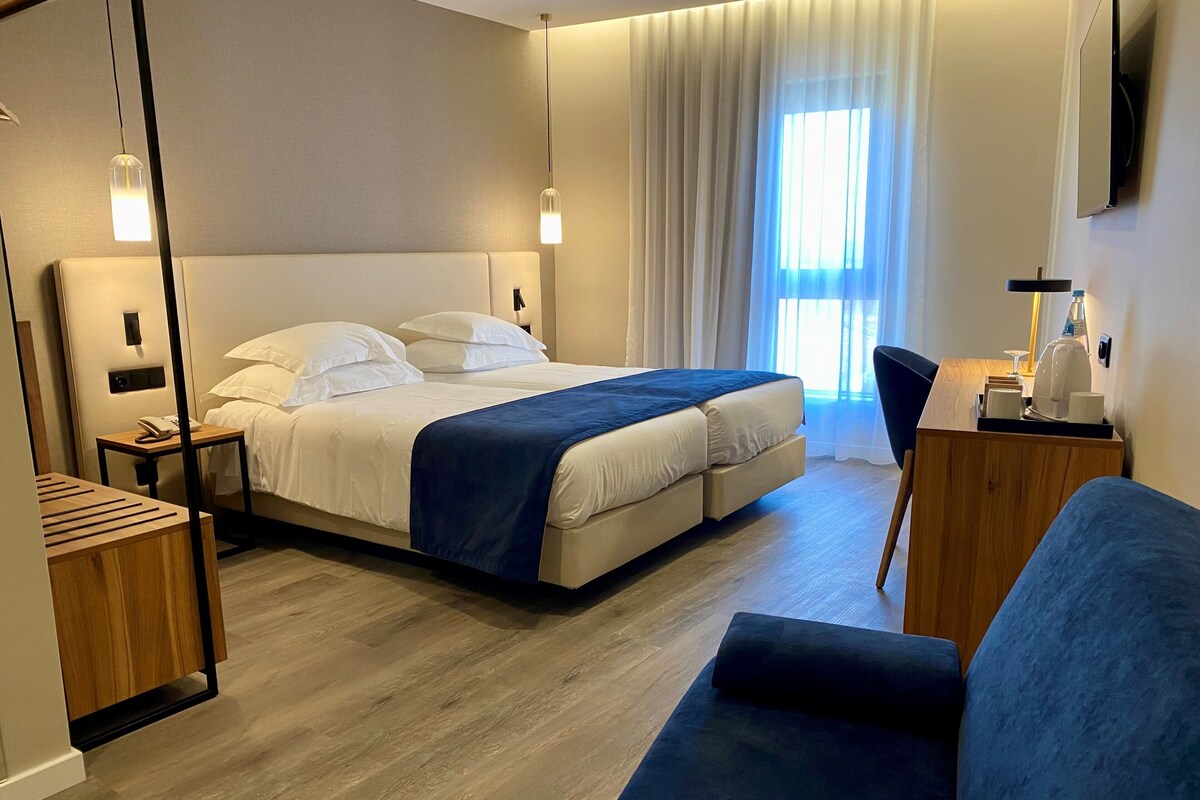 Una habitación de hotel moderna con una cama grande, mesitas de noche, un escritorio y una silla.