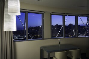 Habitación de hotel moderna con ventanas amplias que ofrecen vista a la ciudad al anochecer.