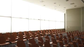 Ein Konferenzraum mit Reihen brauner Stühle, großen Fenstern und einer schlichten Decke mit eingelassener Beleuchtung.