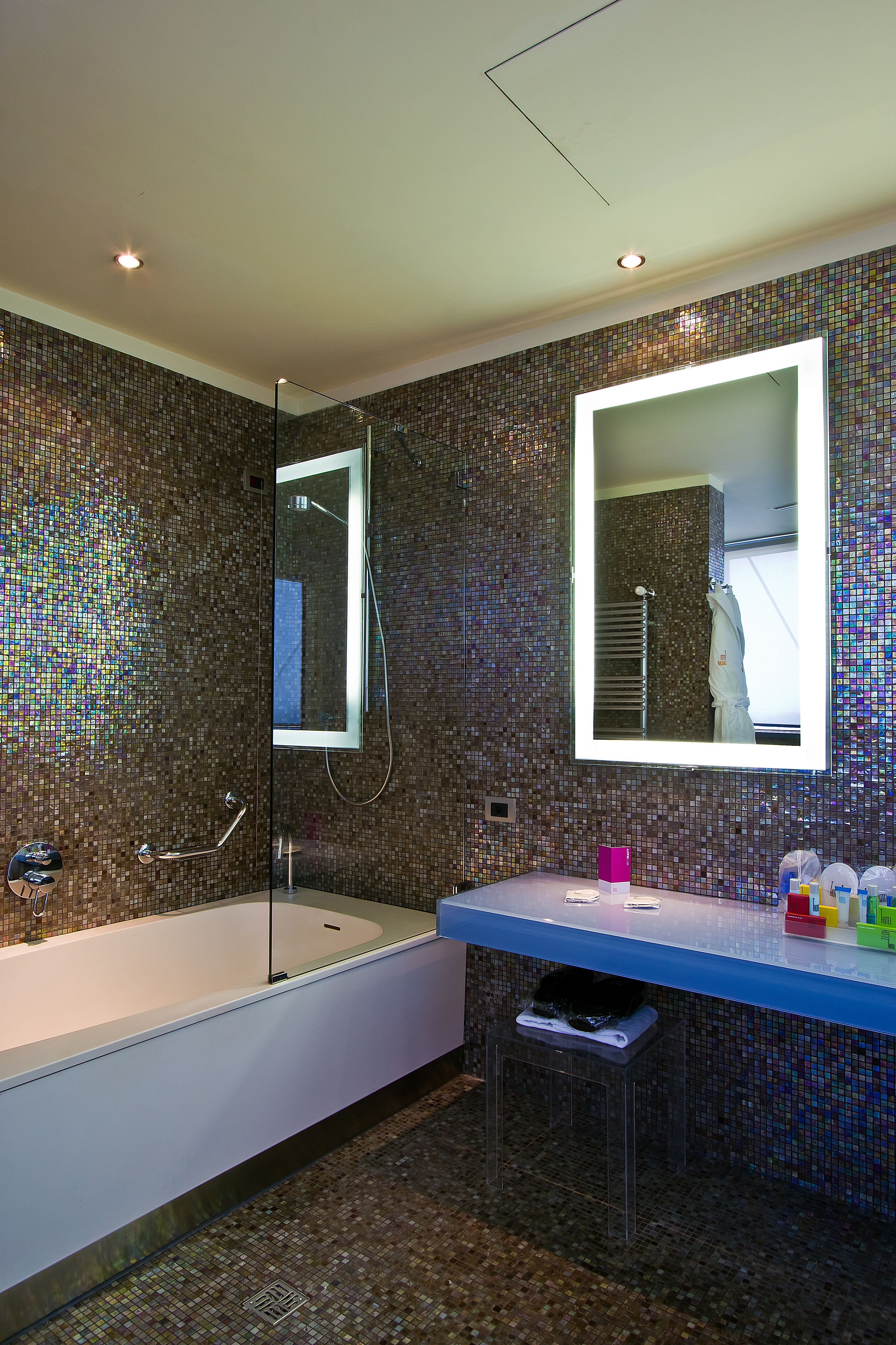 Ein modernes Badezimmer mit einer gläsernen Duschkabine, einem großen Spiegel und einer blauen Ablage mit Toilettenartikeln.