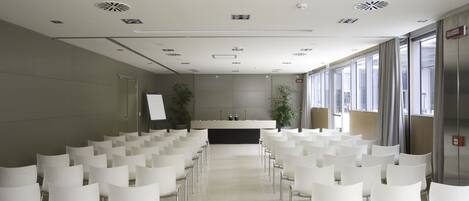 Un salón de conferencias con filas de sillas blancas, un atril y una pizarra.