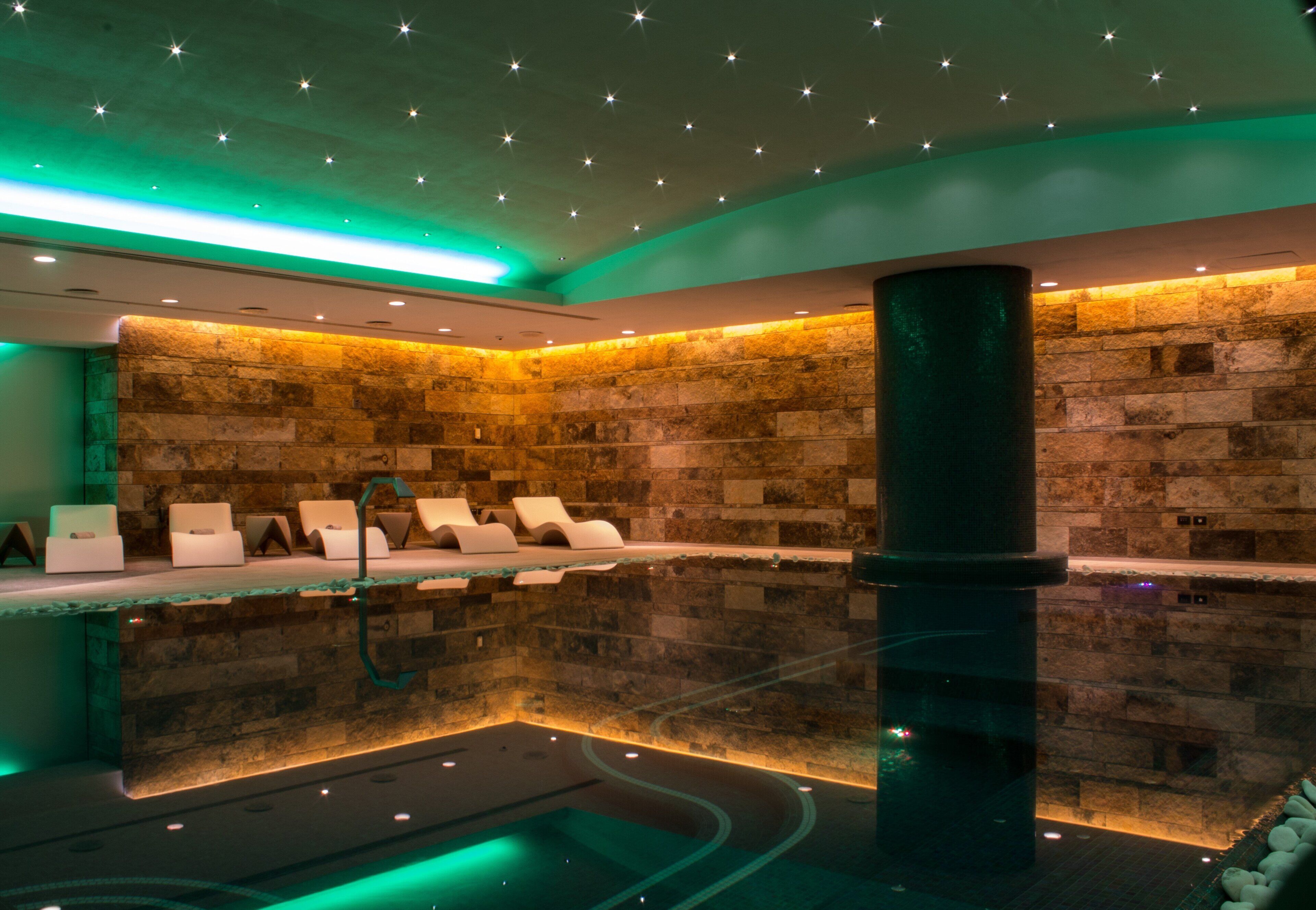 A spa area with a stone wall, a pool, and several lounge chairs.