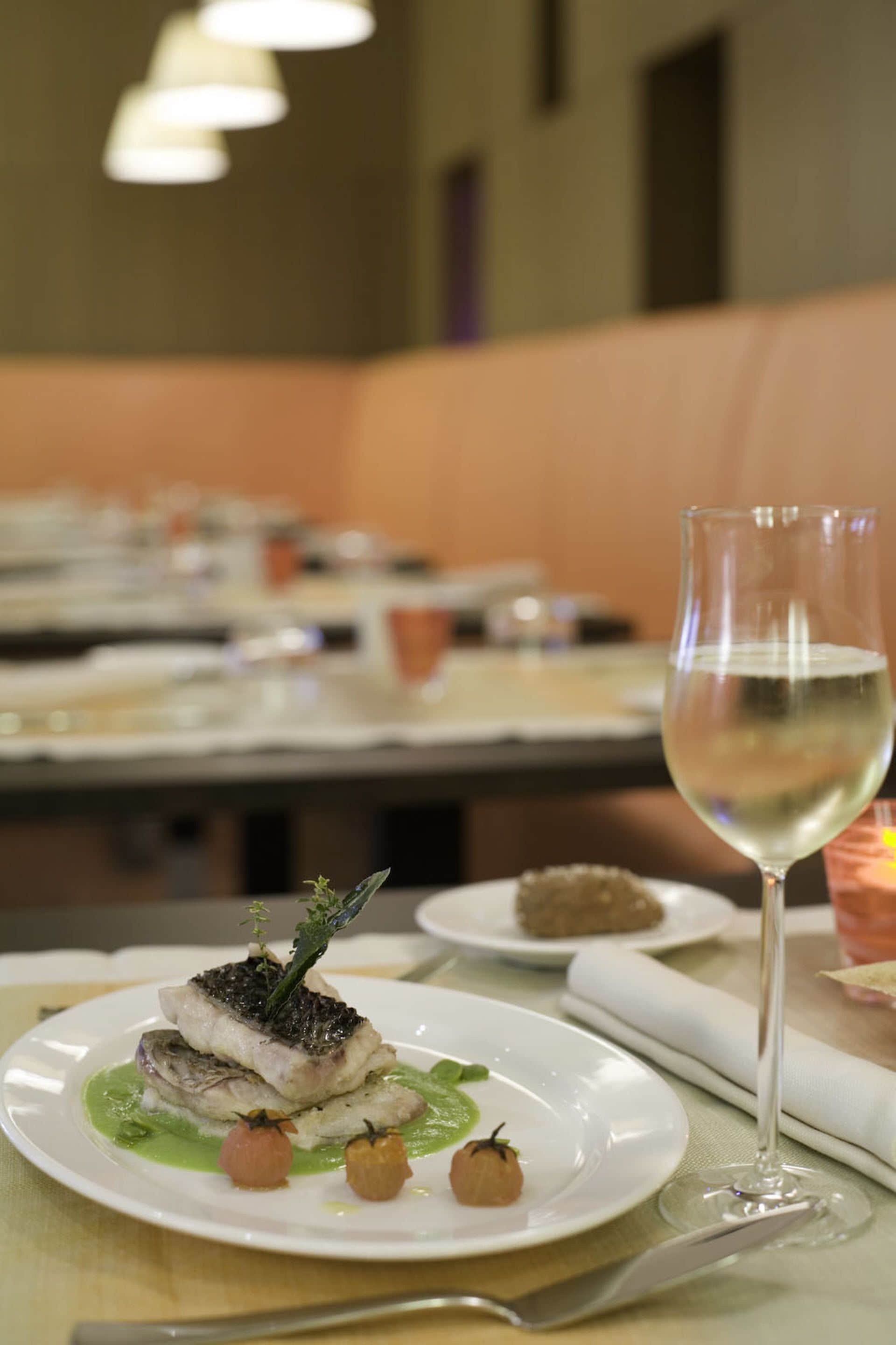 Une table à manger avec une assiette de nourriture, un verre de vin blanc et une fourchette.