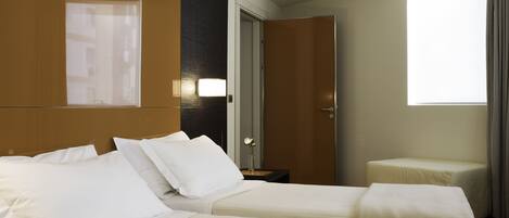 A hotel room with two beds, a nightstand, a lamp, a window, and a door.