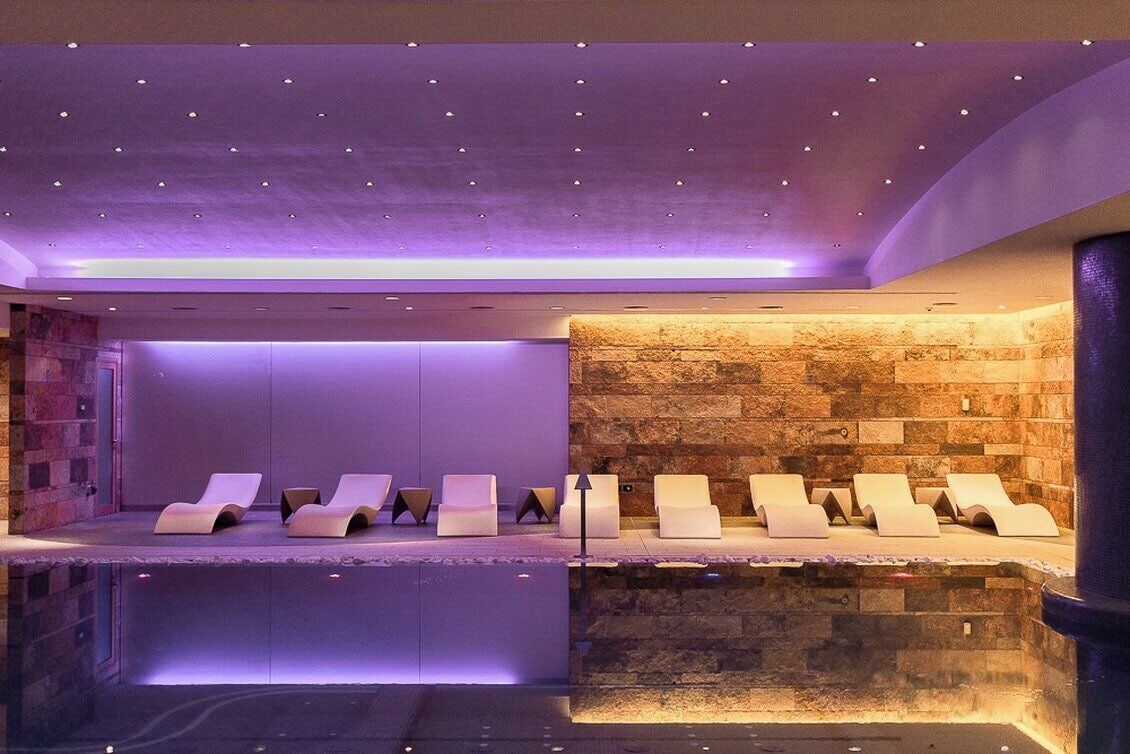 Un área de spa con múltiples sillas reclinables dispuestas a lo largo de una pared de piedra, bajo un techo con iluminación empotrada.