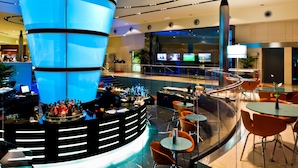 Un espace bar moderne doté d’un éclairage bleu central, de sièges et d’une rambarde en verre.