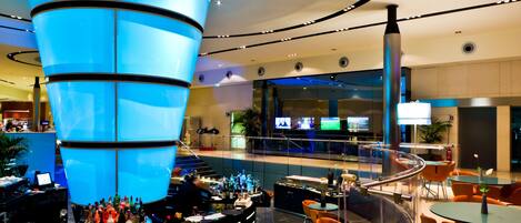 A modern bar area with a central blue light feature, seating, and a glass railing.