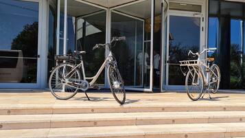 Dos bicicletas estacionadas frente a un edificio con puertas de vidrio y escalones que conducen a la entrada.