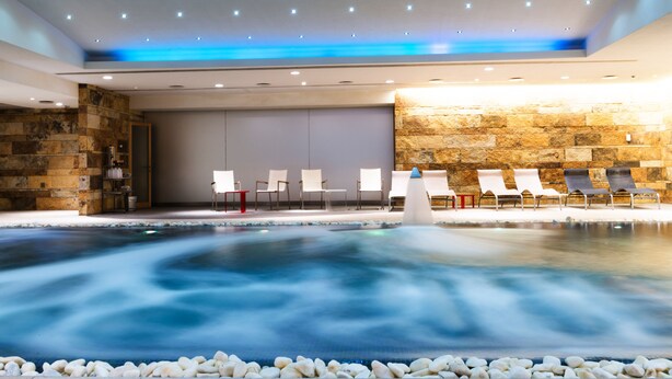 Un espace spa comprenant un jacuzzi, des chaises blanches et un mur en pierre.