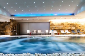 Un espace spa comprenant un jacuzzi, des chaises blanches et un mur en pierre.