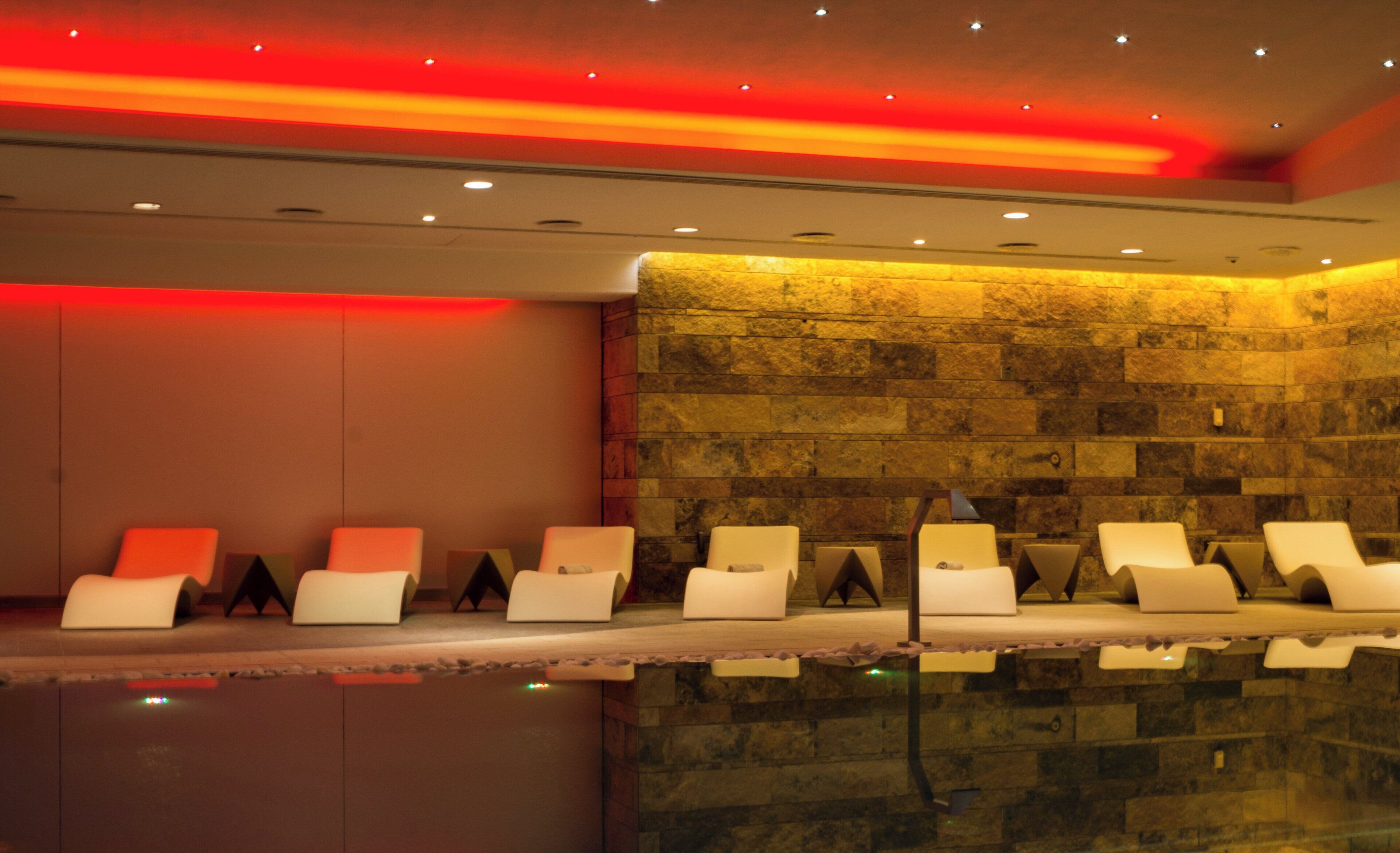 A spa area with multiple white lounge chairs arranged in a row, a stone wall, and a ceiling with red lighting.