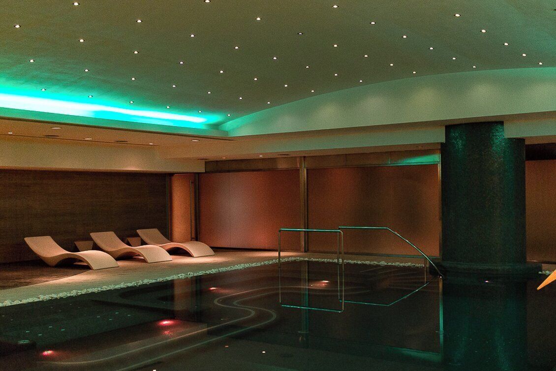 Una piscina interior moderna con sillas de descanso y un separador de vidrio.