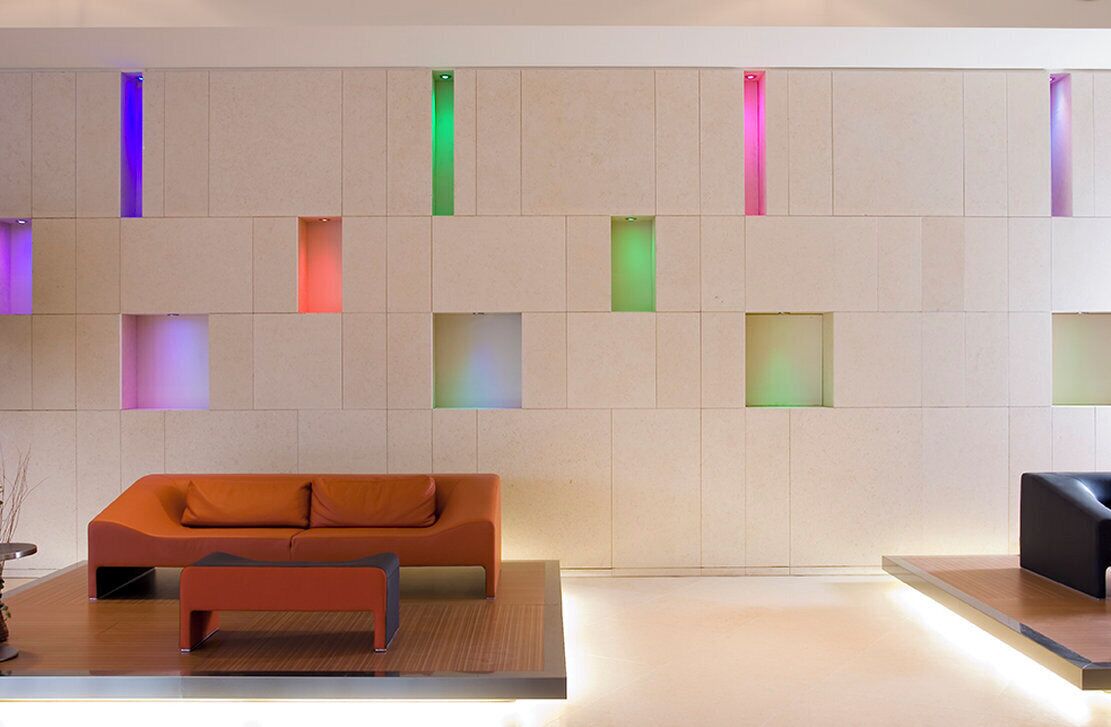 Un'accoglienza moderna con divano e panca, una parete piastrellata illuminata con luci colorate e un design pulito e minimalista.