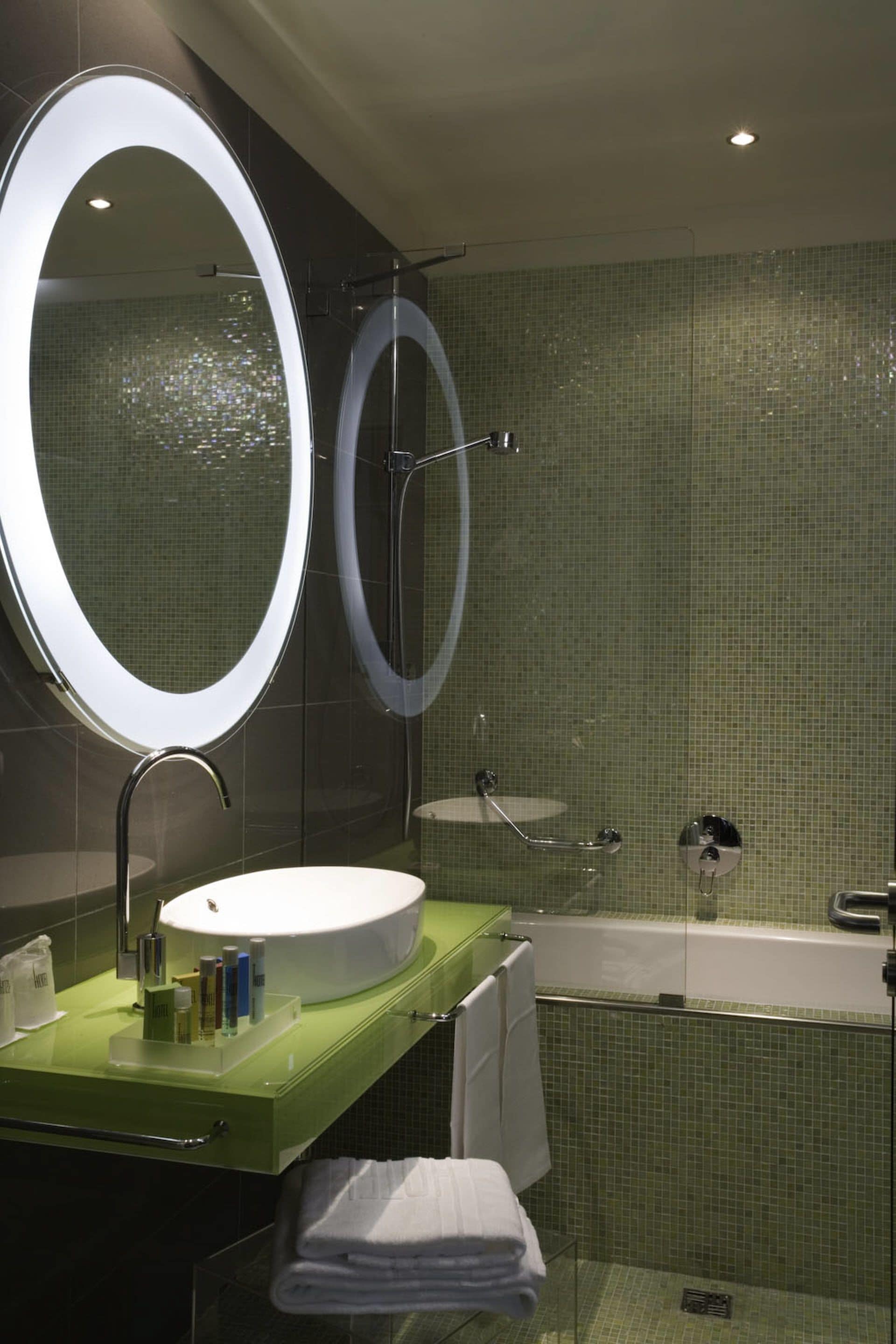 A modern bathroom with a round mirror, a sink, and a bathtub.
