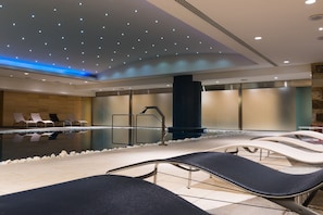 Un área de piscina interior moderna con sillones de descanso, una piscina y un borde de piedra.