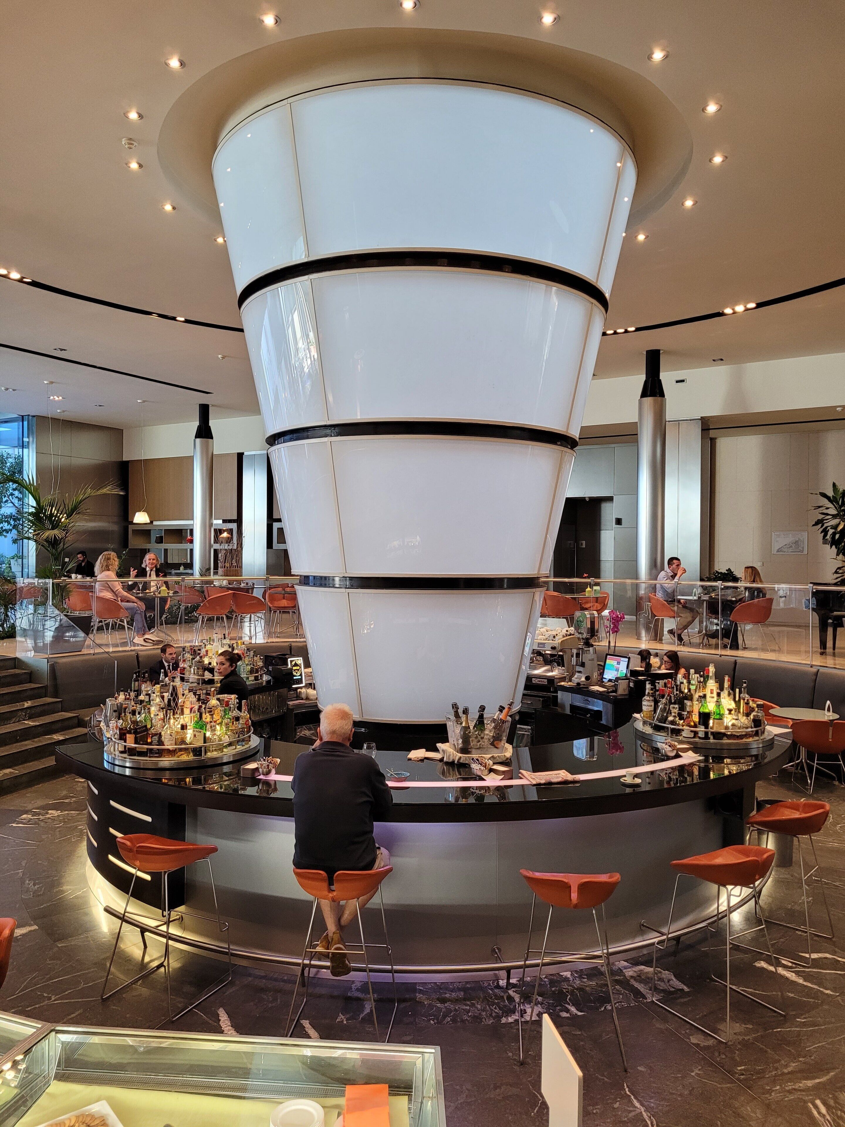 A modern bar area with a central circular structure, seating around the bar, and a glass display case at the front.