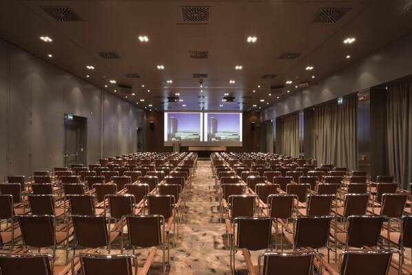 A conference room with rows of chairs, a projector screen, and a carpeted floor.