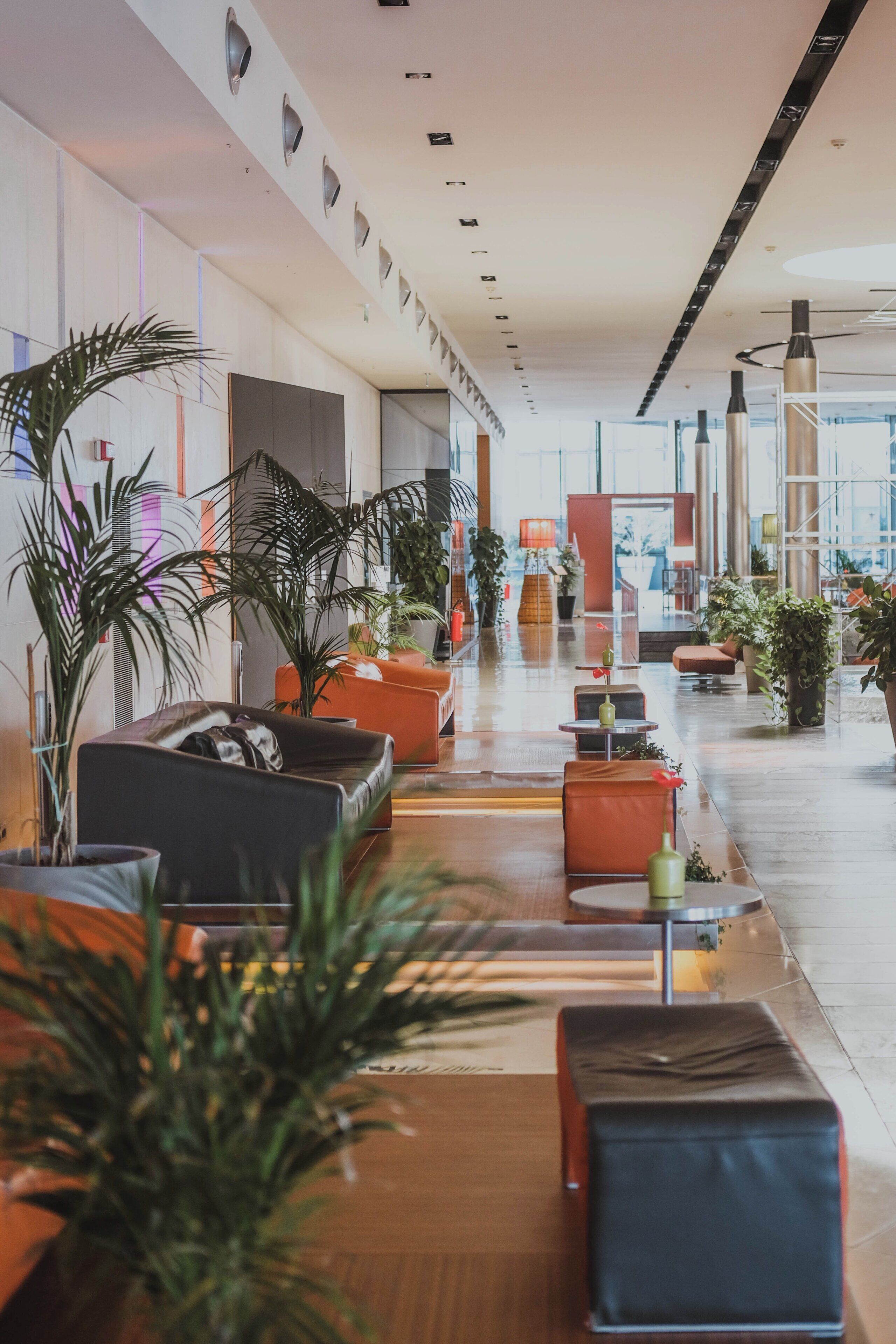 A spacious lobby with seating areas, potted plants, and a modern architectural design.