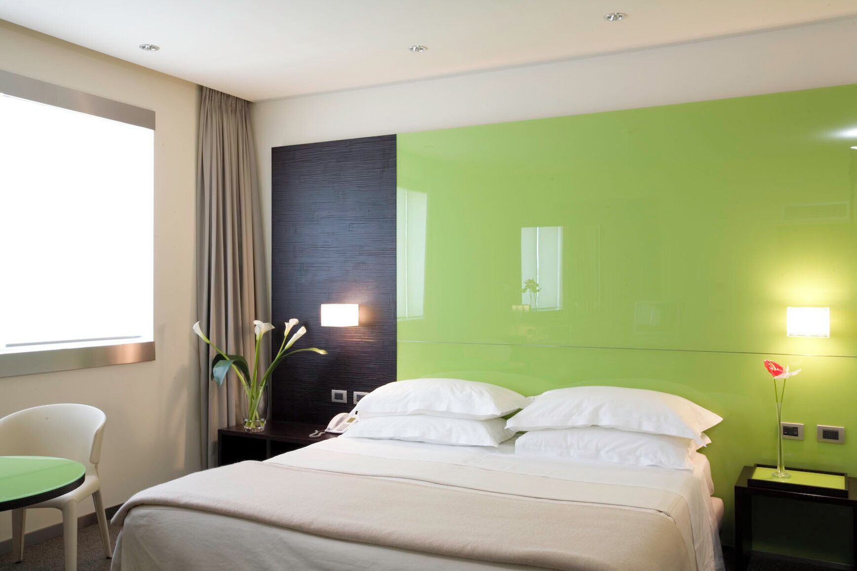 Een hotelkamer met een bed, een bureau, een stoel, een raam en een groene accentmuur.
