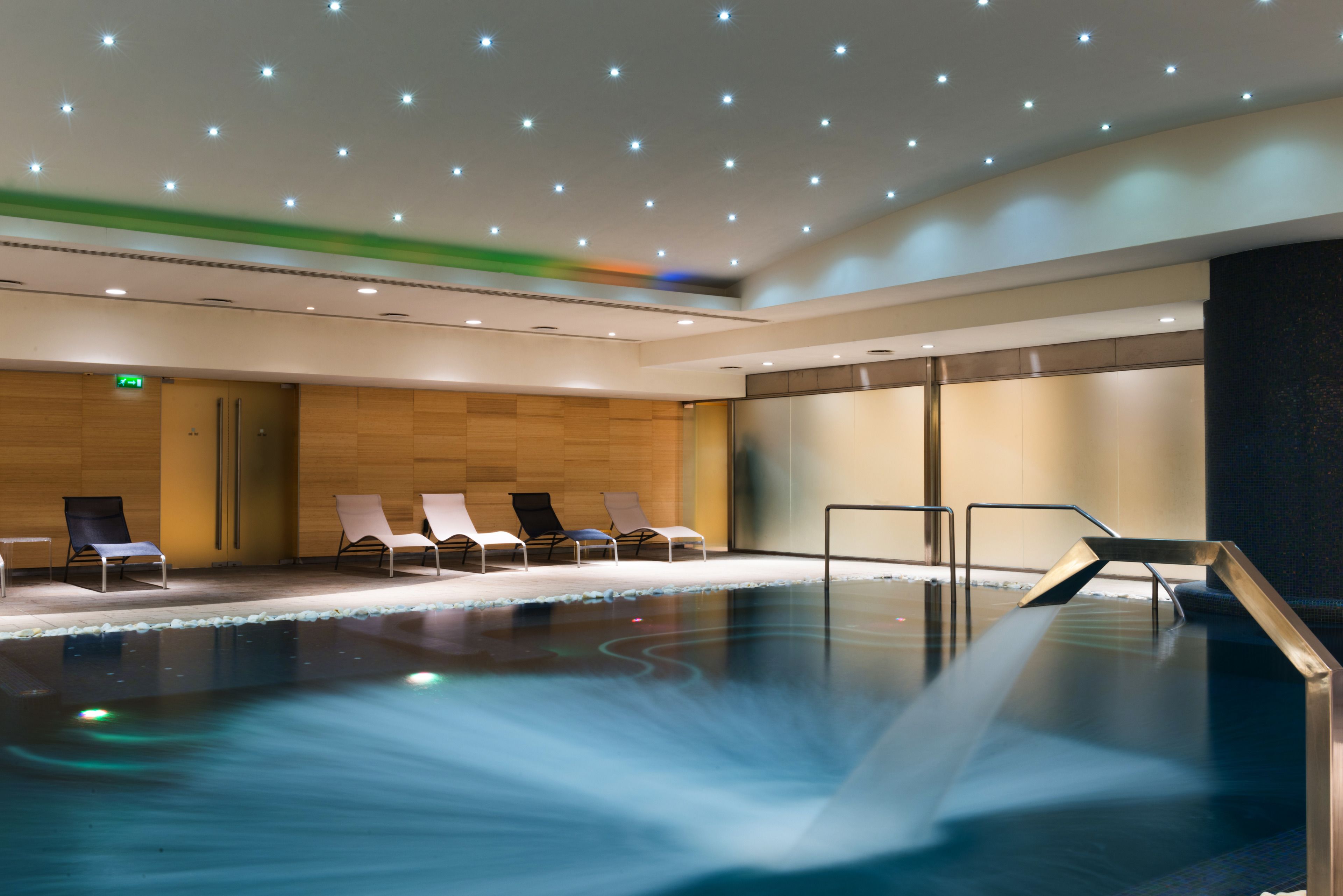 A modern indoor pool area with lounge chairs and a water feature.