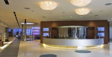 A modern hotel lobby with a reception desk, large windows, and contemporary lighting fixtures.