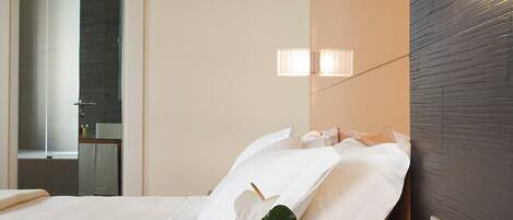 A hotel room with a bed, a bedside table with a vase, a wall-mounted light, and a mirror.