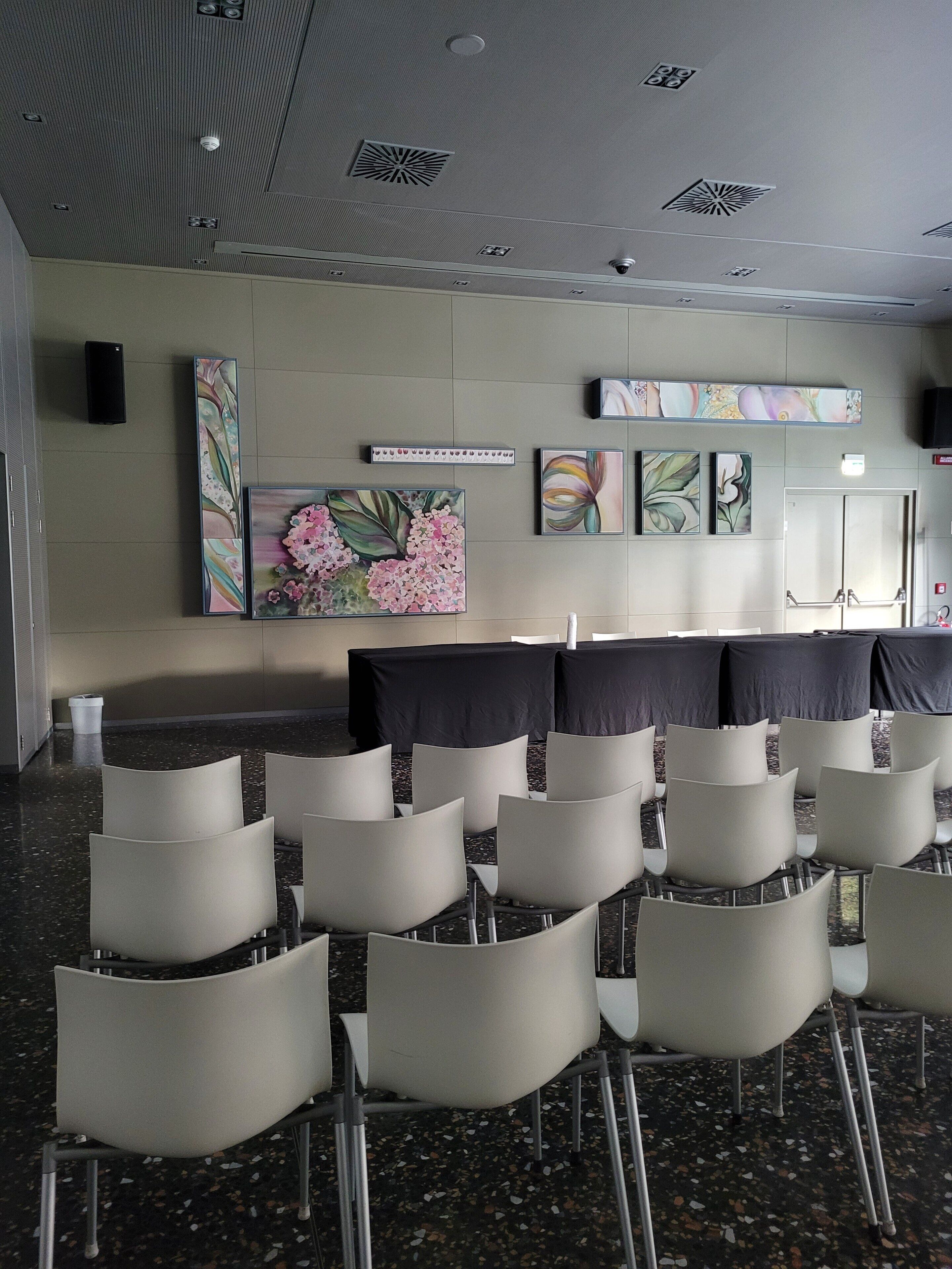 Ein Konferenzraum mit Reihen von Stühlen, einem großen Blumenbild und einem Rauchmelder an der Decke.