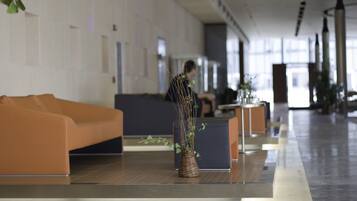 Un lobby moderno con una recepción, una zona de estar con un sofá naranja y una planta decorativa en una cesta tejida.