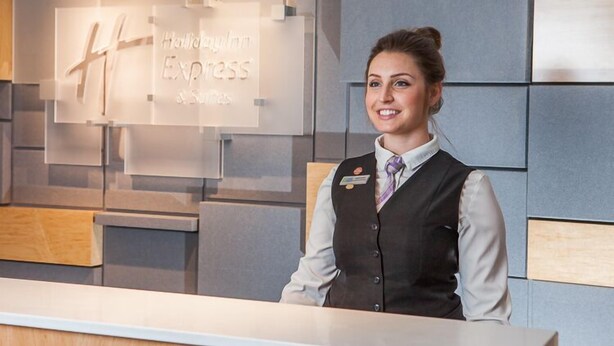 A hotel reception desk with a modern design, featuring a clear glass panel with the hotel's name and logo. - Holiday Inn Express Saint John Harbour Side by IHG (Saint John)