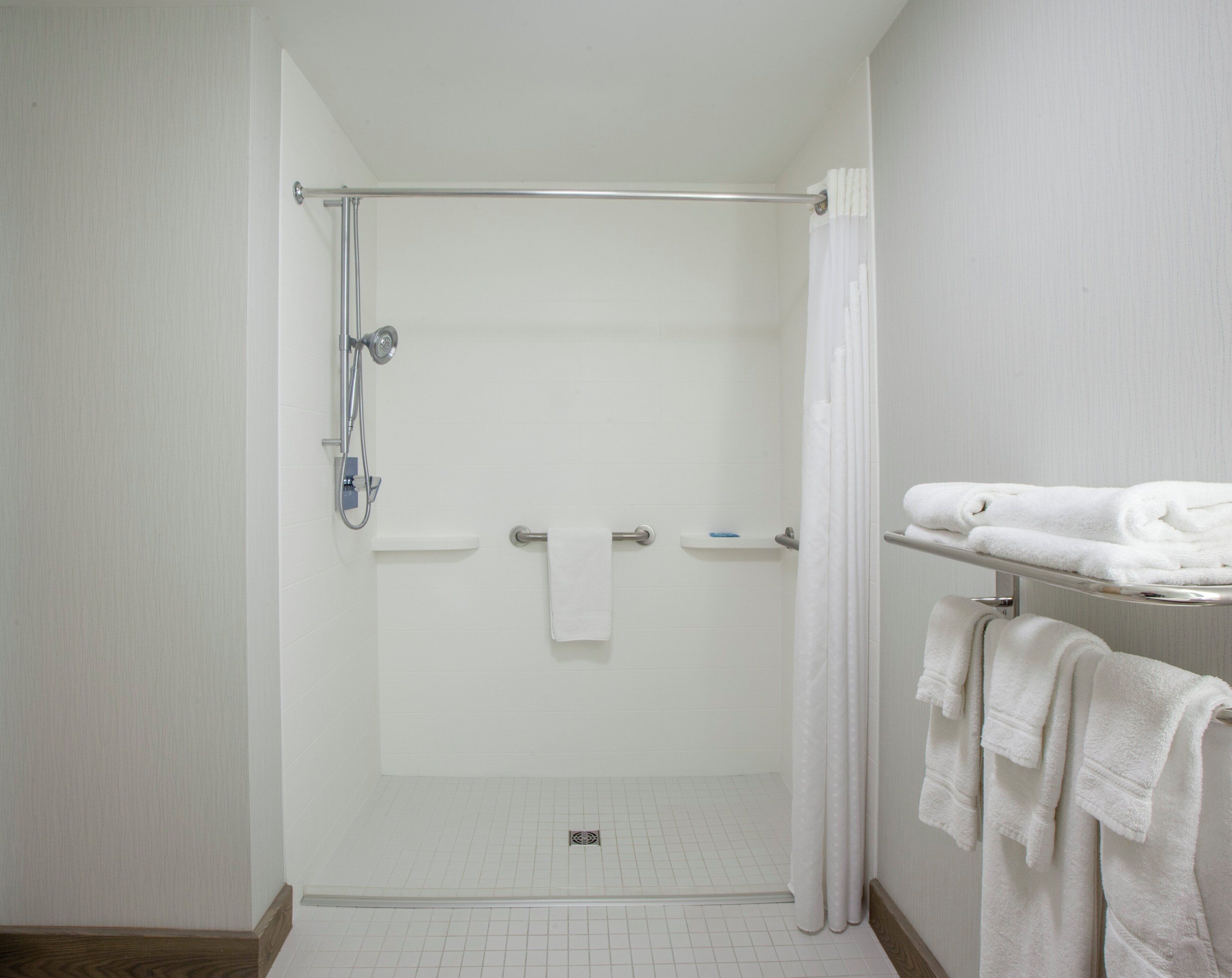 A shower area with a glass door, a towel rack with folded towels, and a showerhead.